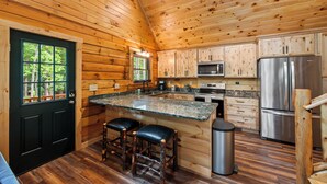 Cocina de cabaña de madera con una isla central, armarios de madera, electrodomésticos de acero inoxidable y una puerta negra con ventana.