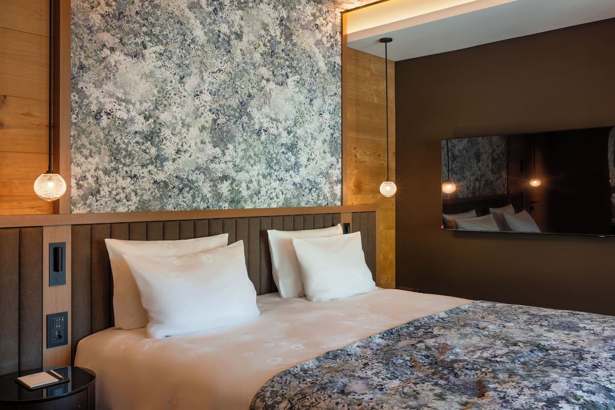 A modern hotel room with a large bed, wooden headboard, and a textured wall.