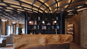 Un comptoir d’accueil en bois, doté d’un grand design incurvé, une bibliothèque remplie de livres et un plafond moderne avec des poutres apparentes et un éclairage design.