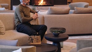 Un homme est assis sur un canapé, avec une cheminée en arrière-plan.