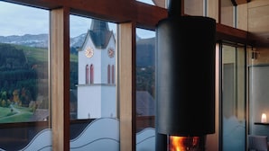 Une pièce chaleureuse avec une cheminée, des sièges confortables et une vue sur une église et des montagnes.