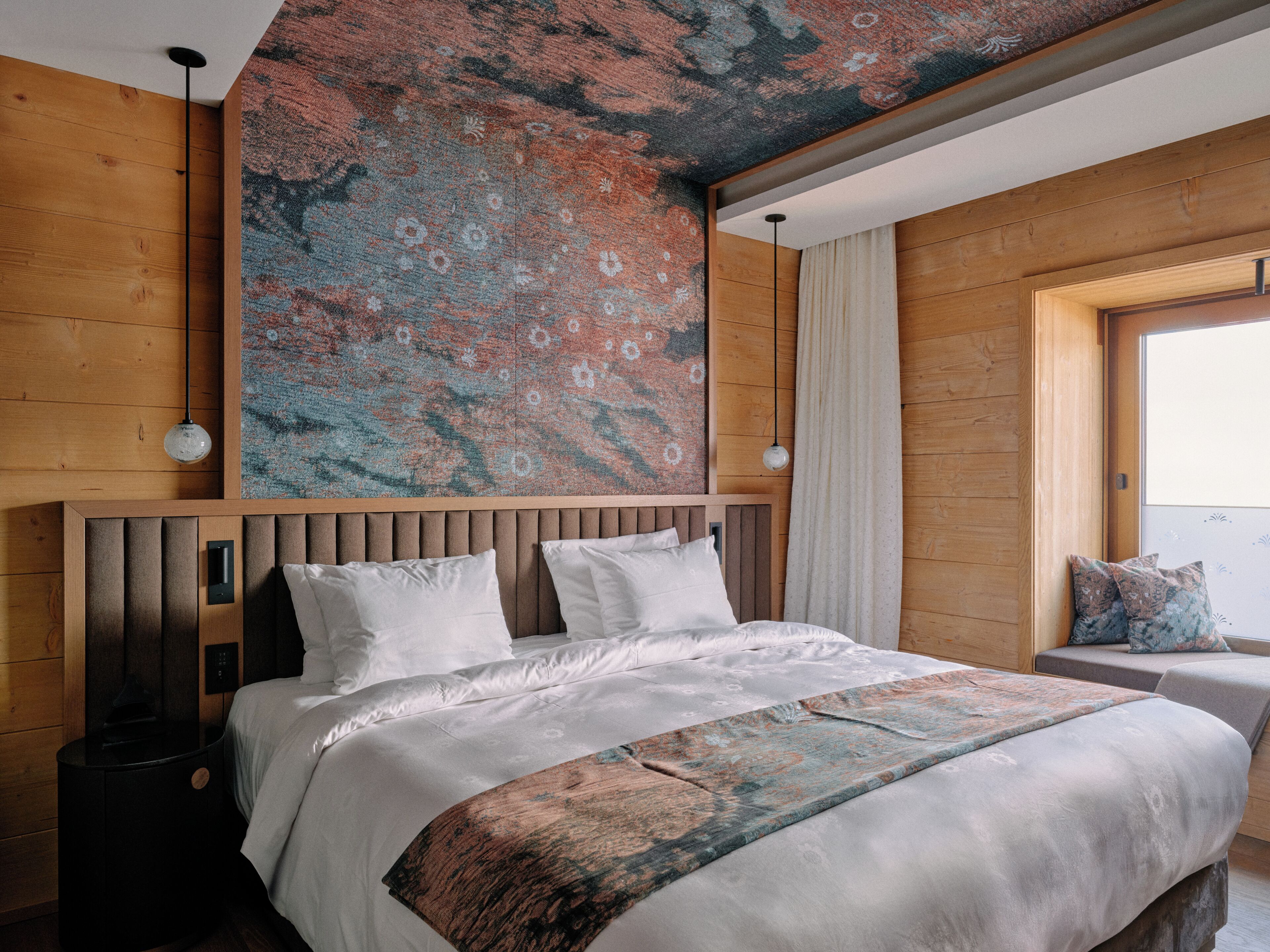 Ein Schlafzimmer mit einem hölzernen Kopfteil, einem großen Bett mit weißer Bettwäsche, einem gemusterten Teppich und einem Fenster mit Vorhängen.