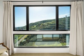A room with a large window overlooking a green hillside.