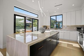 Une cuisine moderne dotée d’un grand îlot central, de meubles blancs et offrant une vue sur un paysage montagneux.