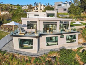 A modern two-story house with a flat roof, large windows, and a glass balcony.