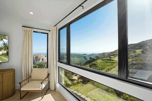 A room with a large window offering a view of green hills and a modern building.