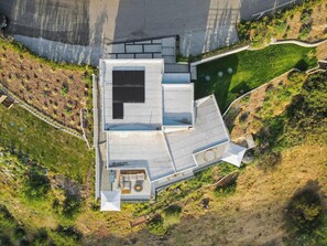 An aerial view of a modern building with a flat roof, a patio area with seating, and a garden surrounding the structure.