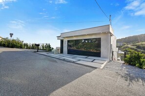 A modern building with a garage entrance, a clear sky, and a hilly landscape in the background.