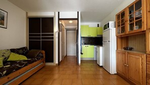 A compact living space with a sofa, a kitchenette, and a wooden cabinet. - Cozy Studio with Pool Access, Private Garden, and Close to Beach - Argelès-sur-Mer (Argelès-sur-Mer)