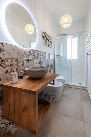 Features a spacious bathroom with a curved mirror, wooden vanity, and glass-enclosed shower.