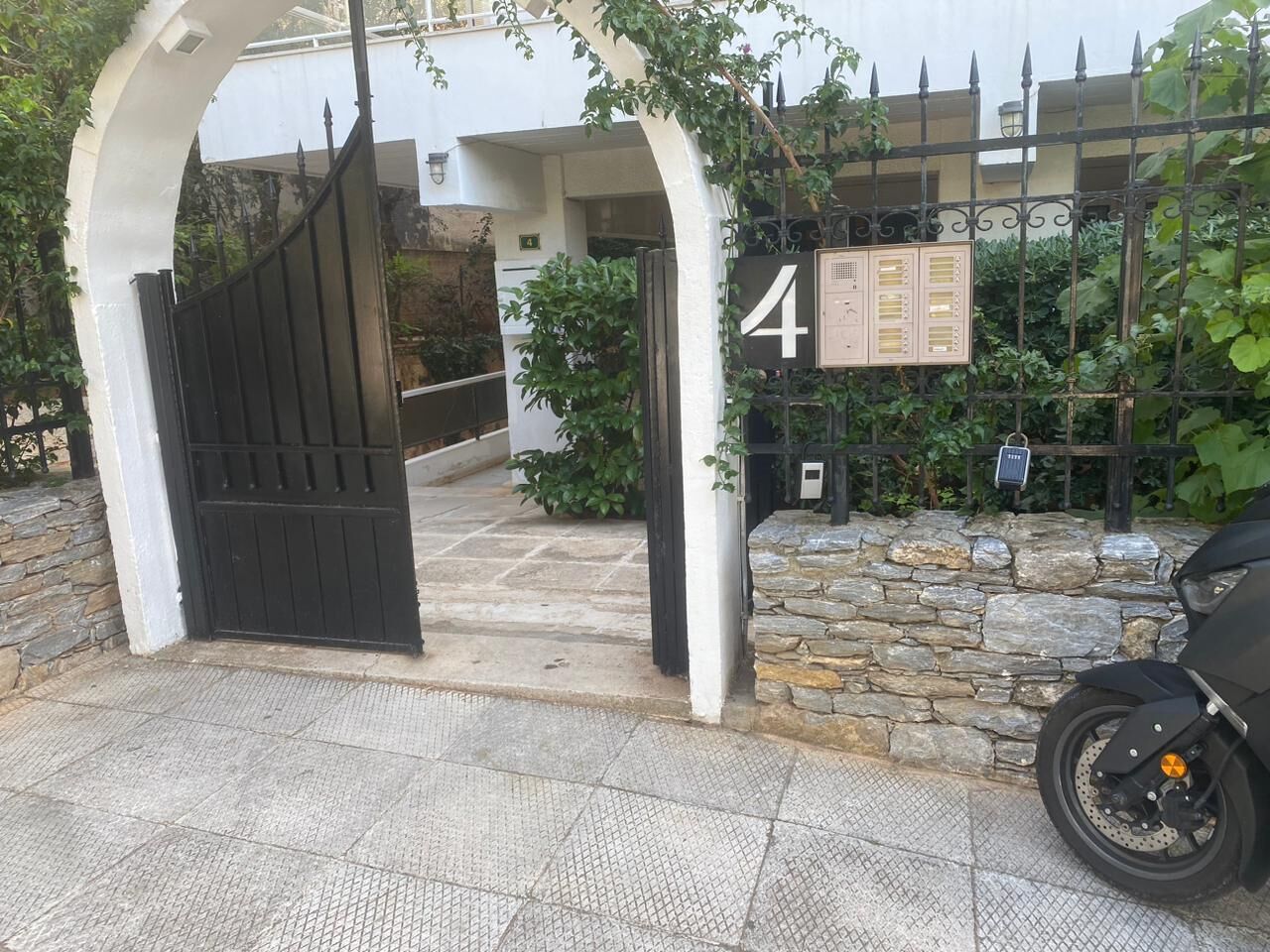 A gated entrance with a stone wall and a motorcycle parked nearby.