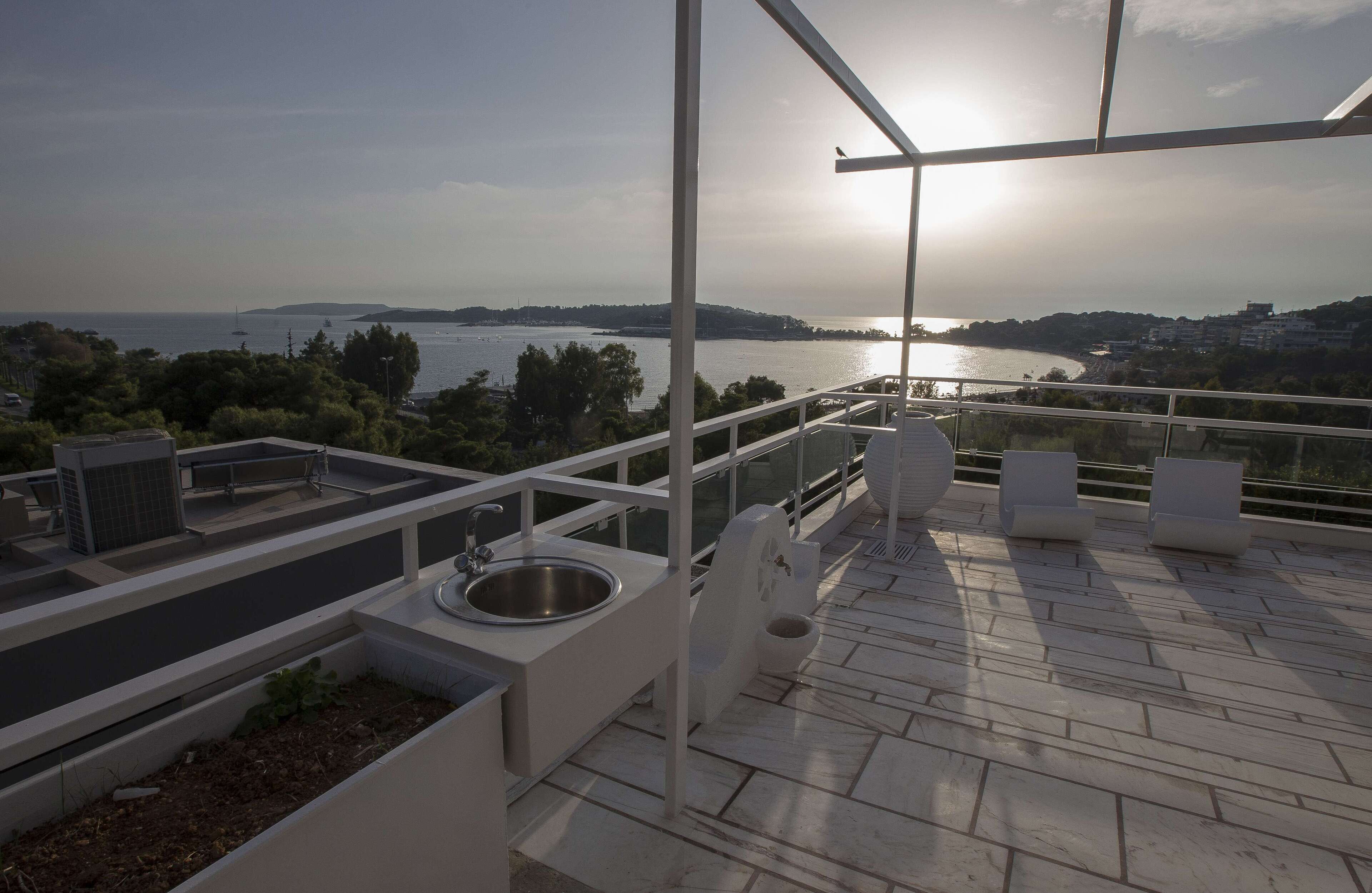 Terraza en la azotea con vistas al mar, un lavamanos y mobiliario de exterior.