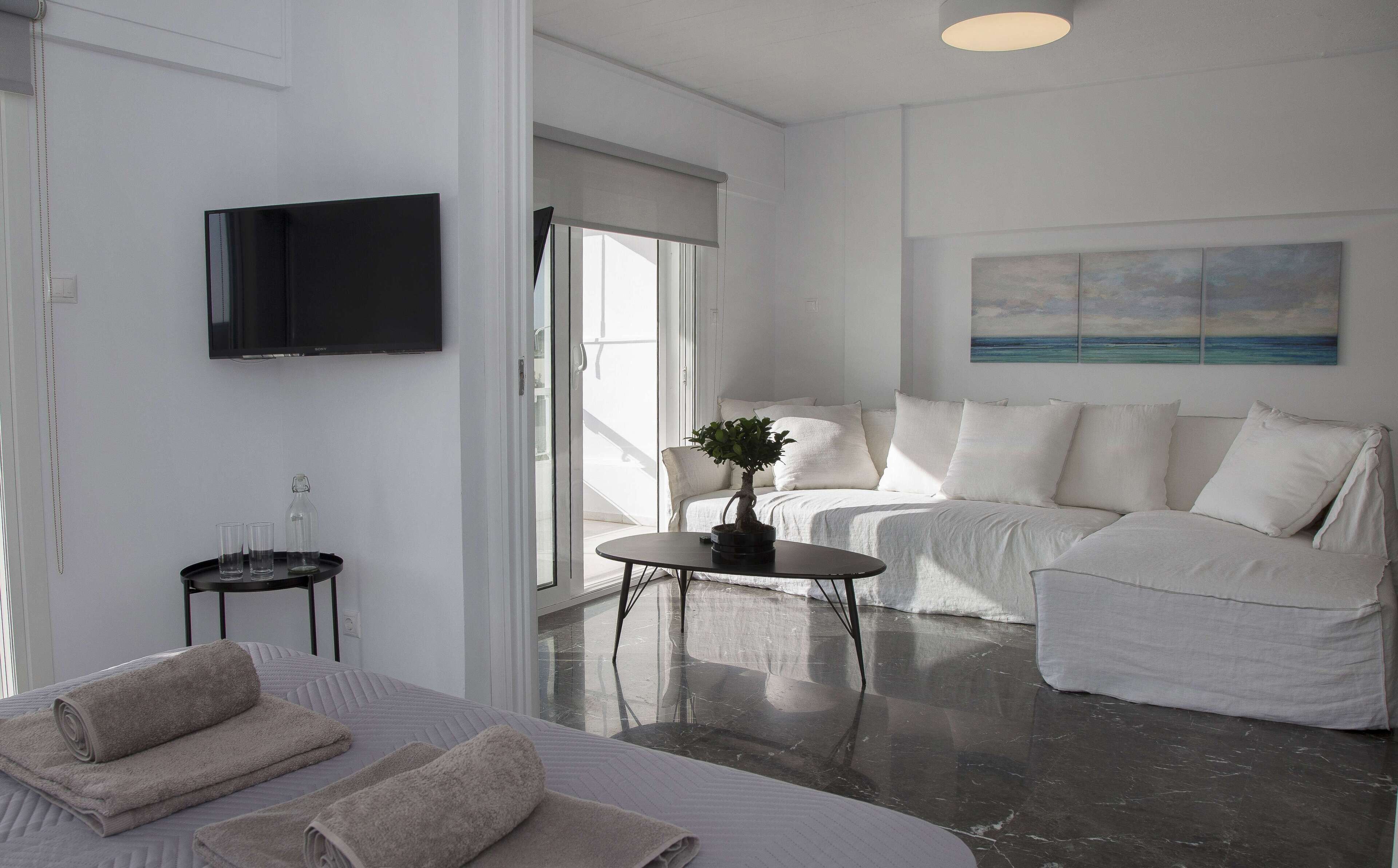 A modern hotel room with a bed, a sofa, a small table with a plant, and a painting on the wall.