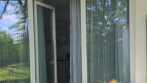 Une petite terrasse avec une table et une chaise, une porte-fenêtre coulissante et une vue sur un jardin.