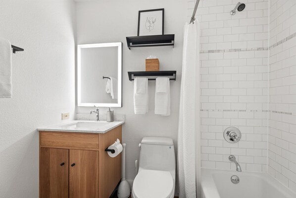 A modern bathroom with a wooden vanity, white sink, toilet, and a shower area with white tiles.