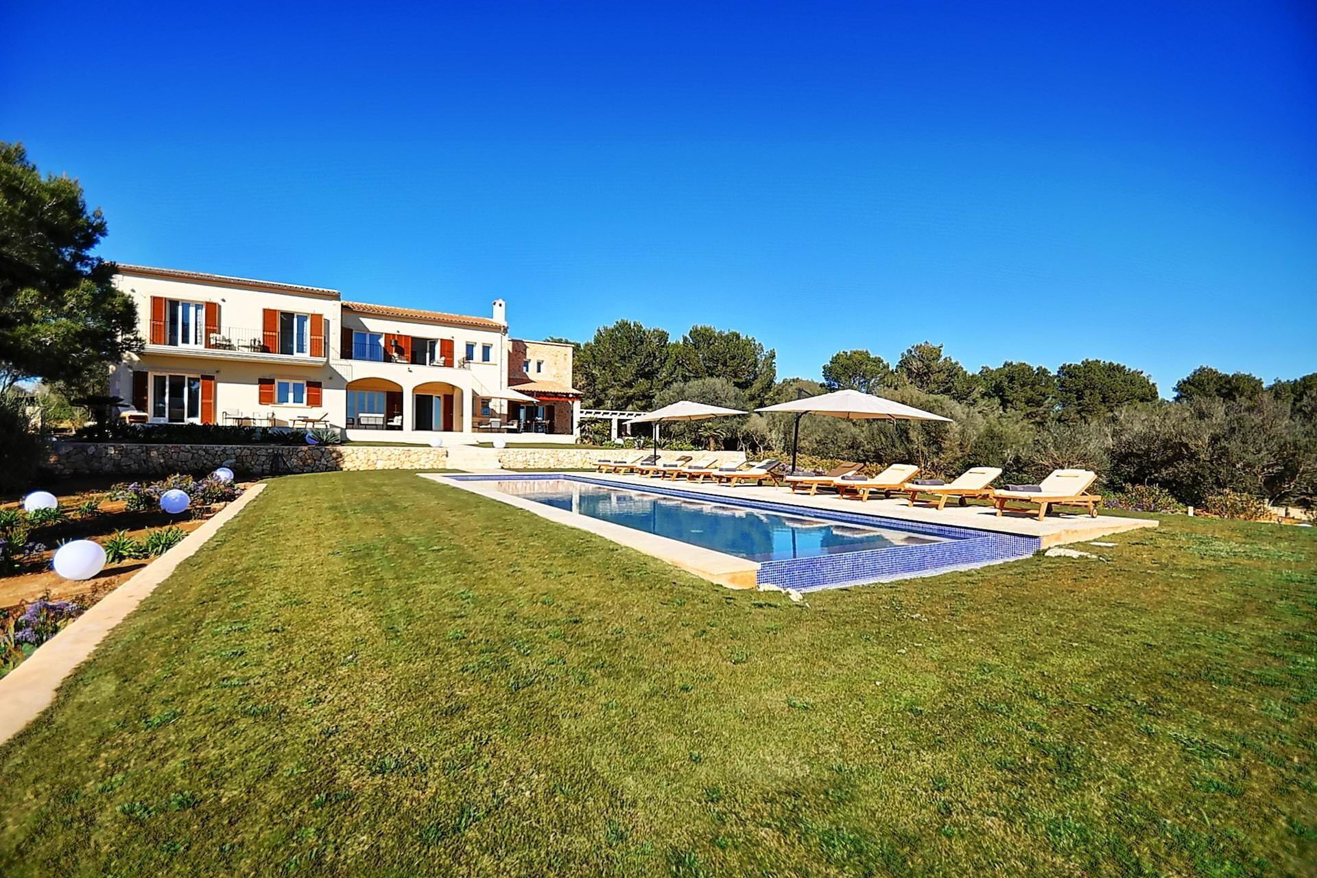 Une maison à deux étages avec une piscine, un espace salon extérieur et un mur en pierre.