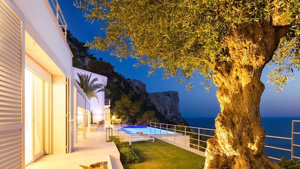 Una casa moderna con piscina, un árbol grande y vista al mar.