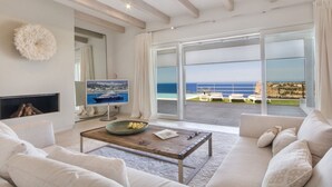 Un salón amplio con un gran ventanal corredera que da a un balcón con vistas al mar.