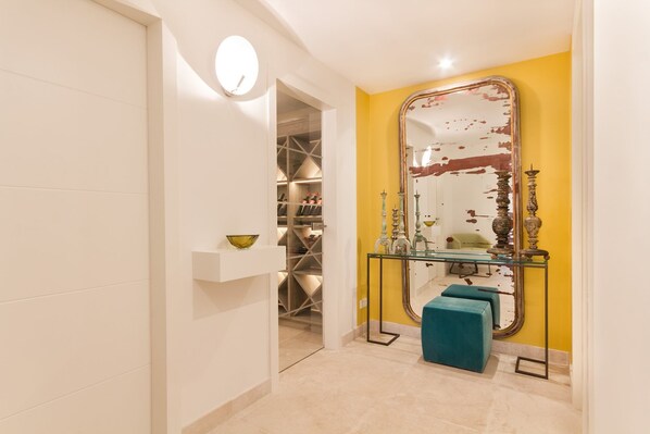 A room with a yellow accent wall, a large mirror, a glass console table, and a teal ottoman.