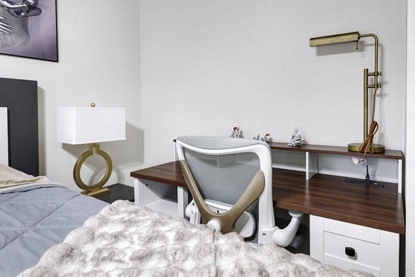 Un dormitorio con una cama, un escritorio con una silla, una lámpara y una estantería en la pared.