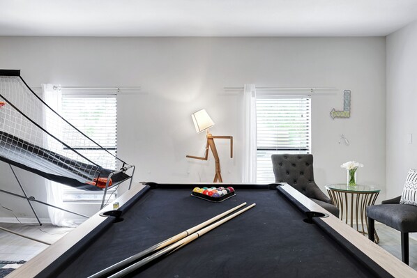 A pool table with a cue stick, a pool ball rack, and a lamp.