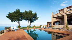 A swimming pool with lounge chairs, a stone building with a balcony, and trees in the background. - My Rental Homes | Villa Gem with sea view and pool (Soller)