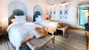 A hotel room with two beds, a woven bench, a patterned rug, and a wardrobe with geometric designs. - My Rental Homes | Villa Gem with sea view and pool (Soller)