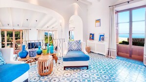 A bright room with a blue patterned floor, a white sofa, and a wooden table with colorful vases. - My Rental Homes | Villa Gem with sea view and pool (Soller)