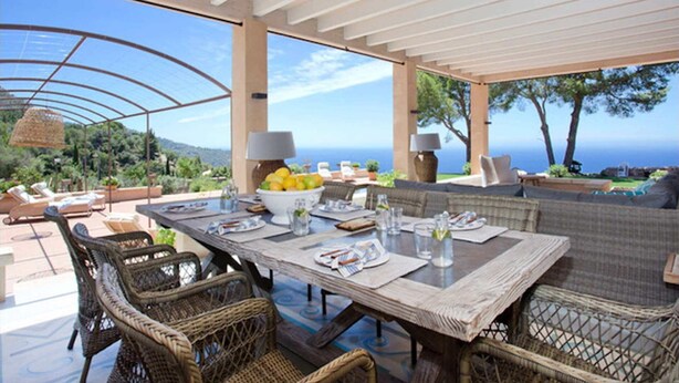 An outdoor dining area with a view of the sea, wicker furniture, and a table set for two. - My Rental Homes | Villa Gem with sea view and pool (Soller)