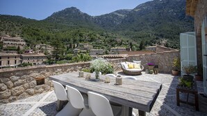 A terrace with a stone wall, a wooden table, and white chairs.
