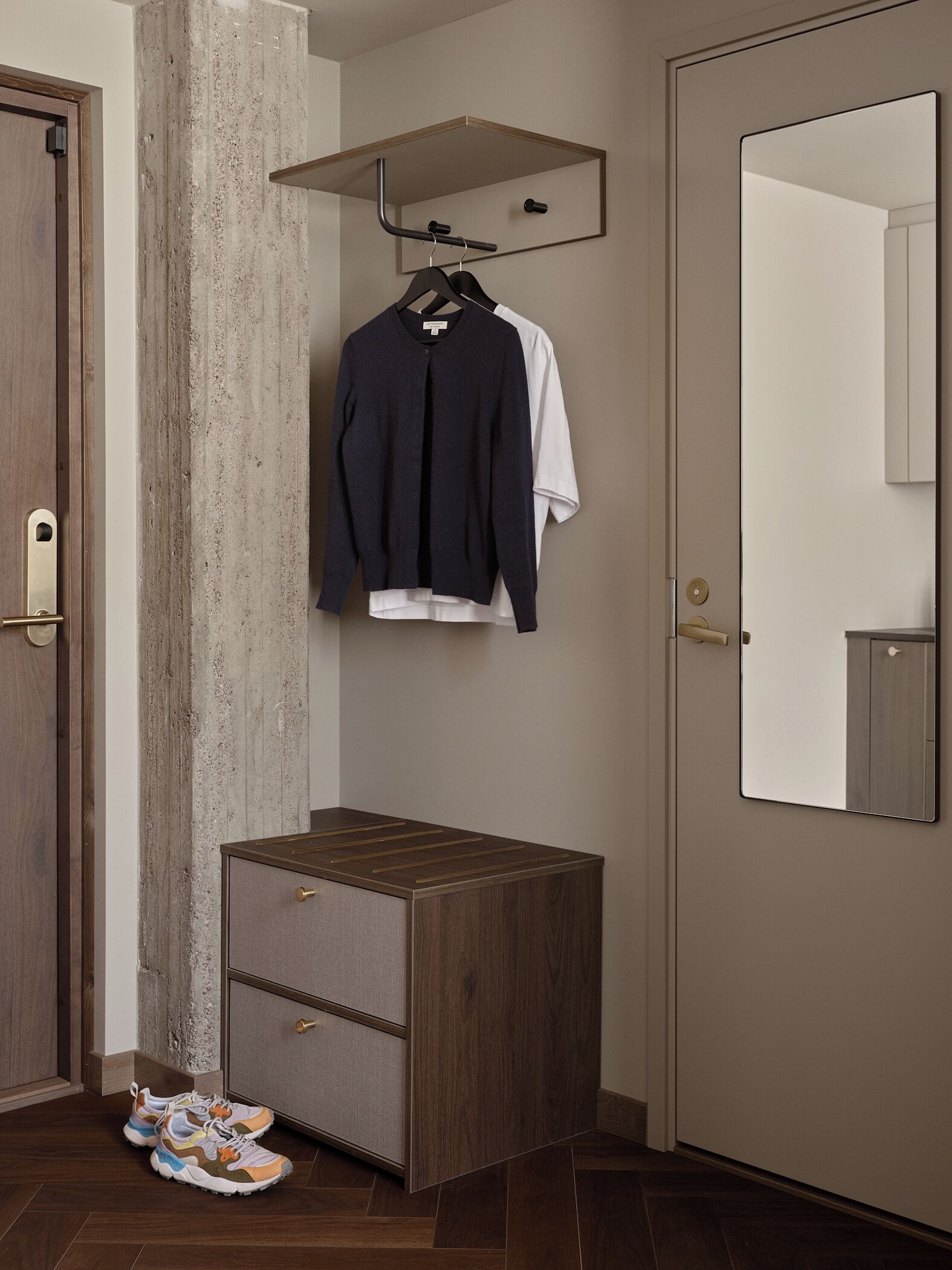 Quarto com um armário de madeira, um espelho e um cabideiro com um suéter escuro e uma camisa branca.