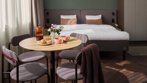 A modern hotel room with a bed, bedside tables, a round dining table with chairs, and a hanging light fixture. - Bob W Helsinki Kamppi (Helsinki)