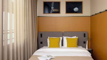 Quarto de hotel com cama, duas almofadas, mesa de cabeceira e janela com cortinas.