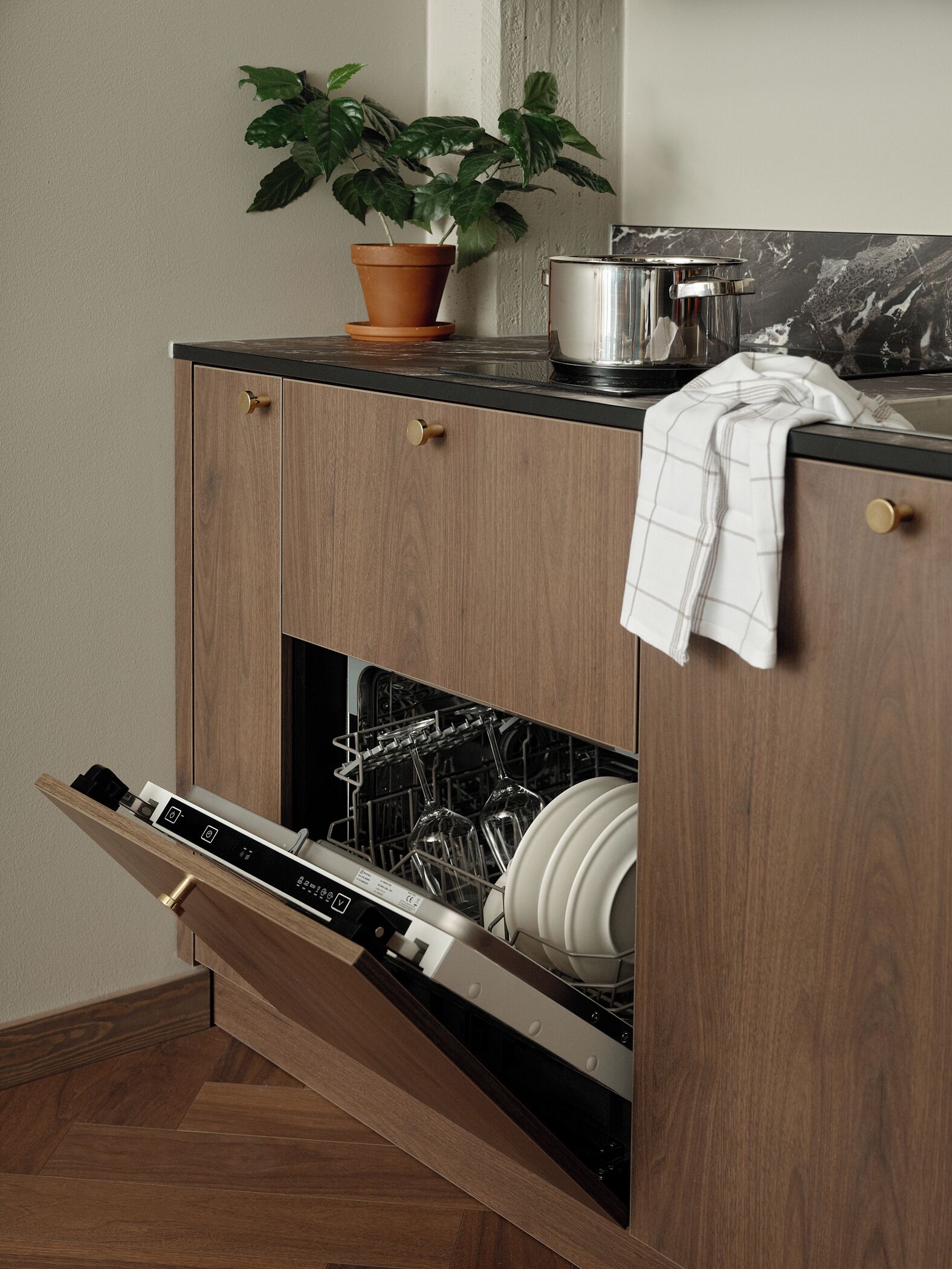 Een keuken met een inbouwvaatwasser, houten kastjes, een potplant en een marmeren spatwand.