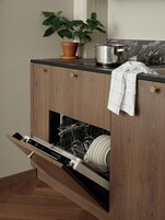 A kitchen with a built-in dishwasher, wooden cabinets, a potted plant, and a marble backsplash.