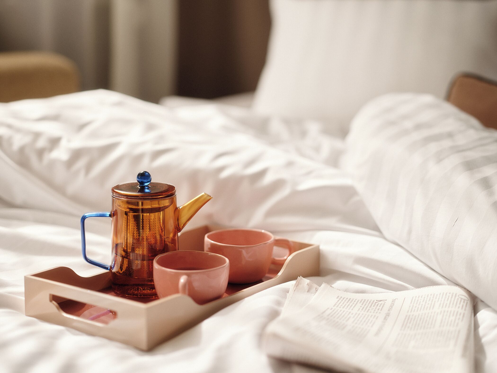 A tray with a teapot and cups on a bed.