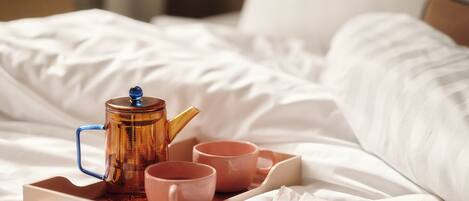 A tray with a teapot and cups on a bed.