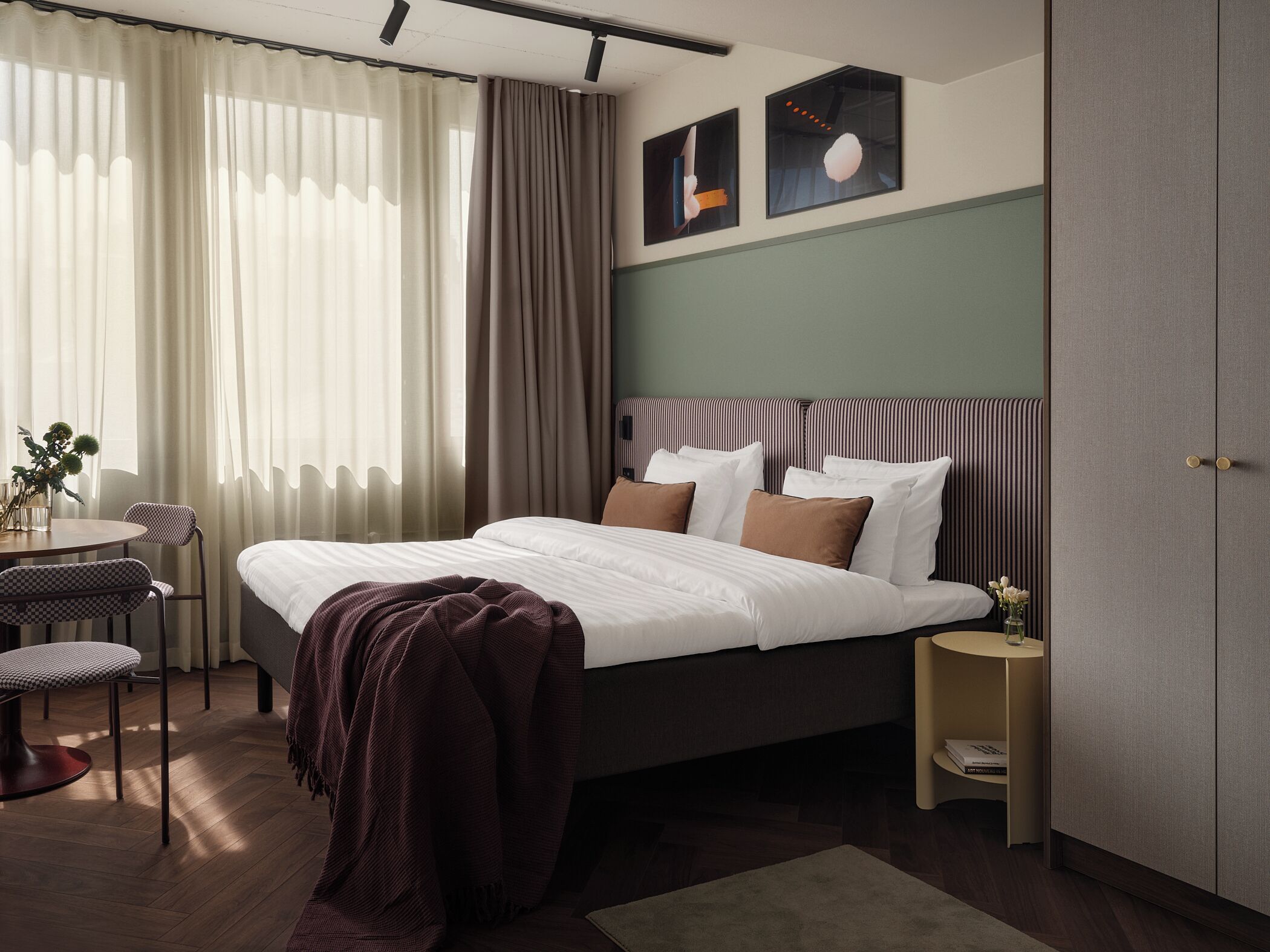 Una camera d'hotel moderna con un letto grande, una scrivania e una sedia. Si notano due quadri alle pareti e un armadio.