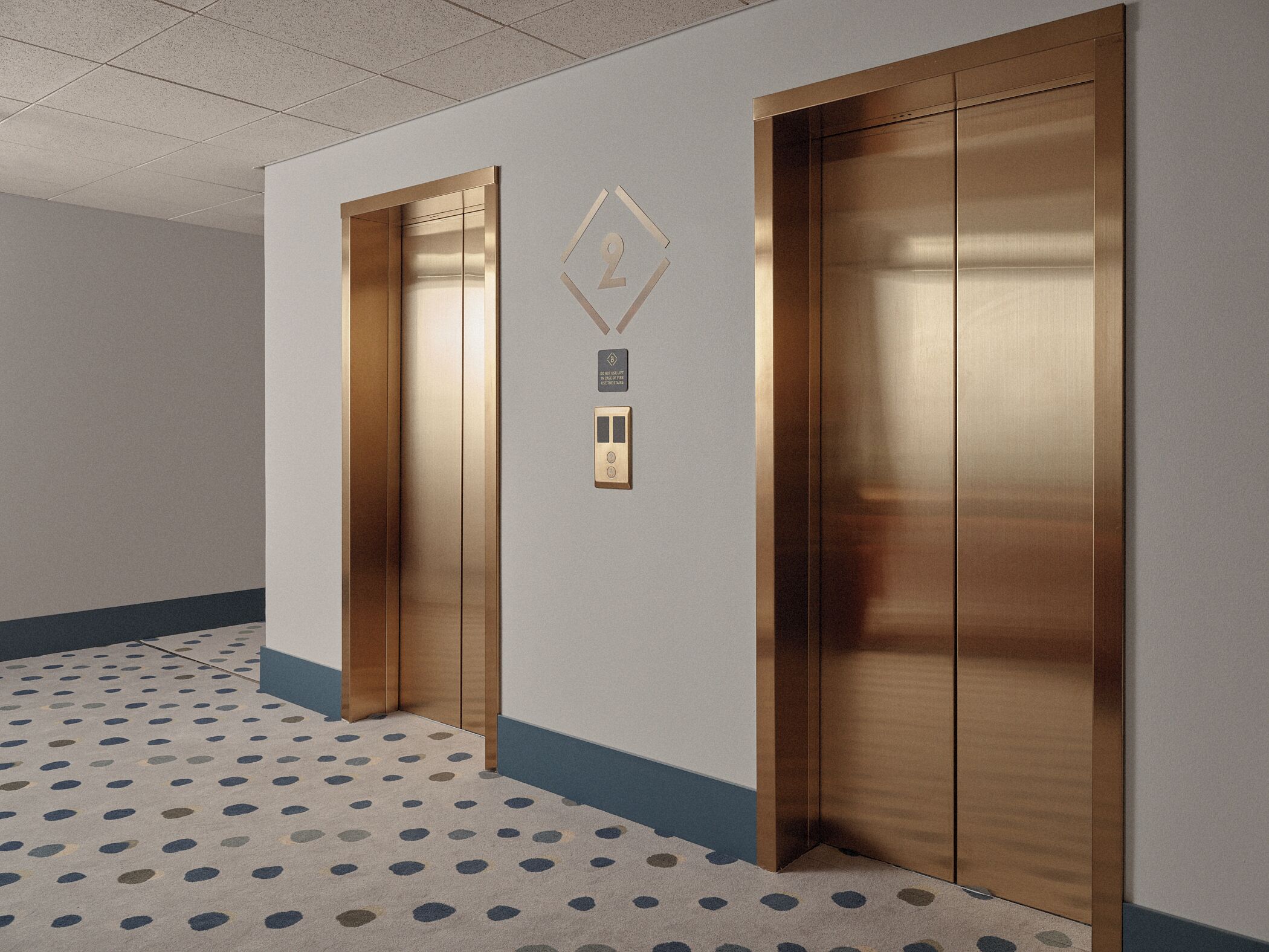 A hallway with two elevators, a patterned carpet, and a wall-mounted sign.