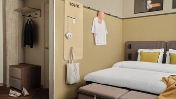 A hotel room with a bed, a bench, a wardrobe, a mirror, and a wall-mounted towel rack.