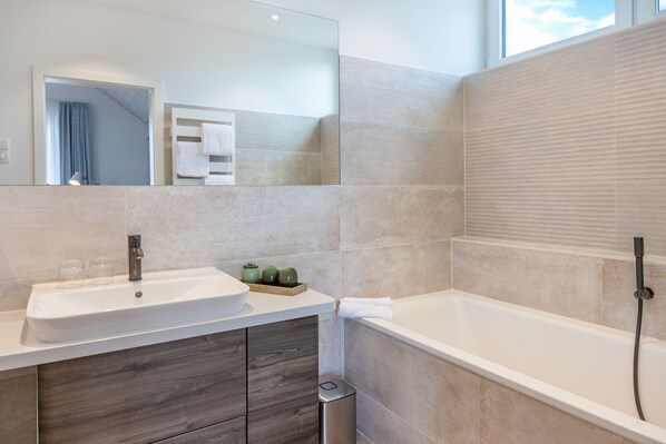 A modern bathroom with a large sink, mirror, and bathtub.