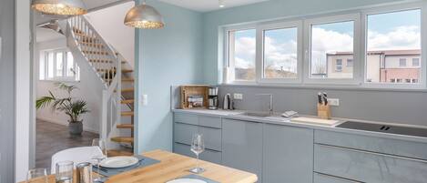 A modern kitchen with a wooden dining table, grey cabinets, and a large window.