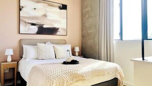A bedroom with a bed, nightstands, a lamp, a painting, and a window with curtains.