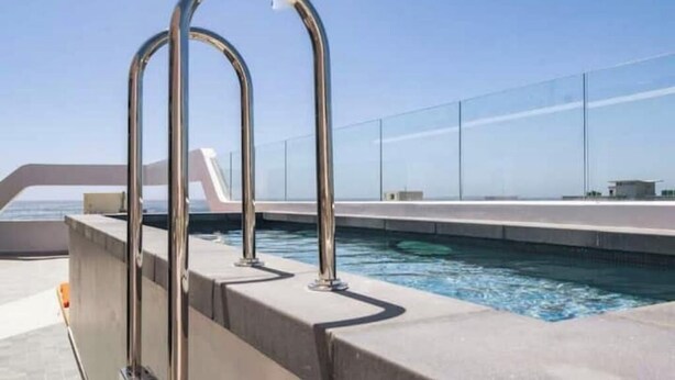 A pool with metal railings and a clear view of the ocean.