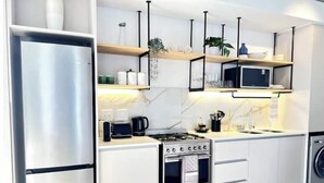 A modern kitchen with white cabinets, a stainless steel refrigerator, a microwave, a stove, and a washing machine.