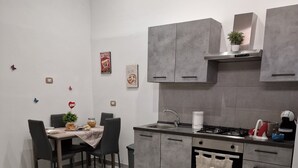 A modern kitchen with grey cabinets, a gas stove, and a dining area with a table and chairs. - Isabel house (Napoli)