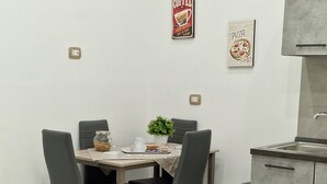 A dining area with a table set for four, a trash bin, and a kitchen area with a sink and cabinets. - Isabel house (Napoli)