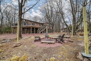 Ein zweistöckiges Gebäude mit einem Balkon, einer Feuerstelle mit Sitzgelegenheiten und einer umliegenden Waldlandschaft.