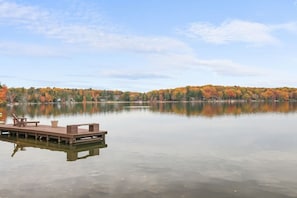 A calm lake with a dock and chairs, surrounded by trees with autumn foliage.