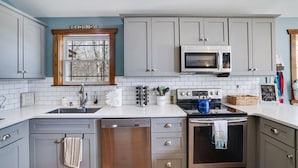 A kitchen with grey cabinets, a microwave, a stove, and a window with a view of trees. - Lakeview Escape with Hot Tub, lake, & Ski (Lake Harmony)